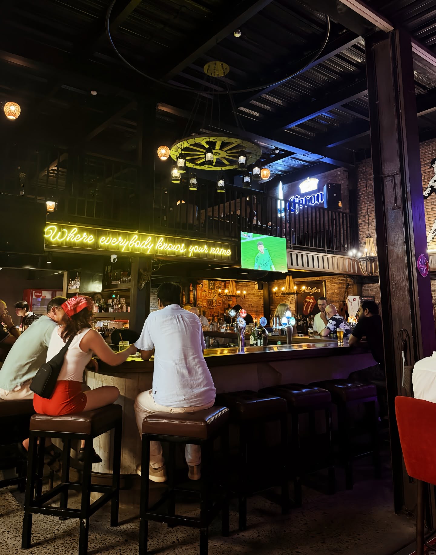 Guests sitting at the Cheers bar beneath the glowing house motto