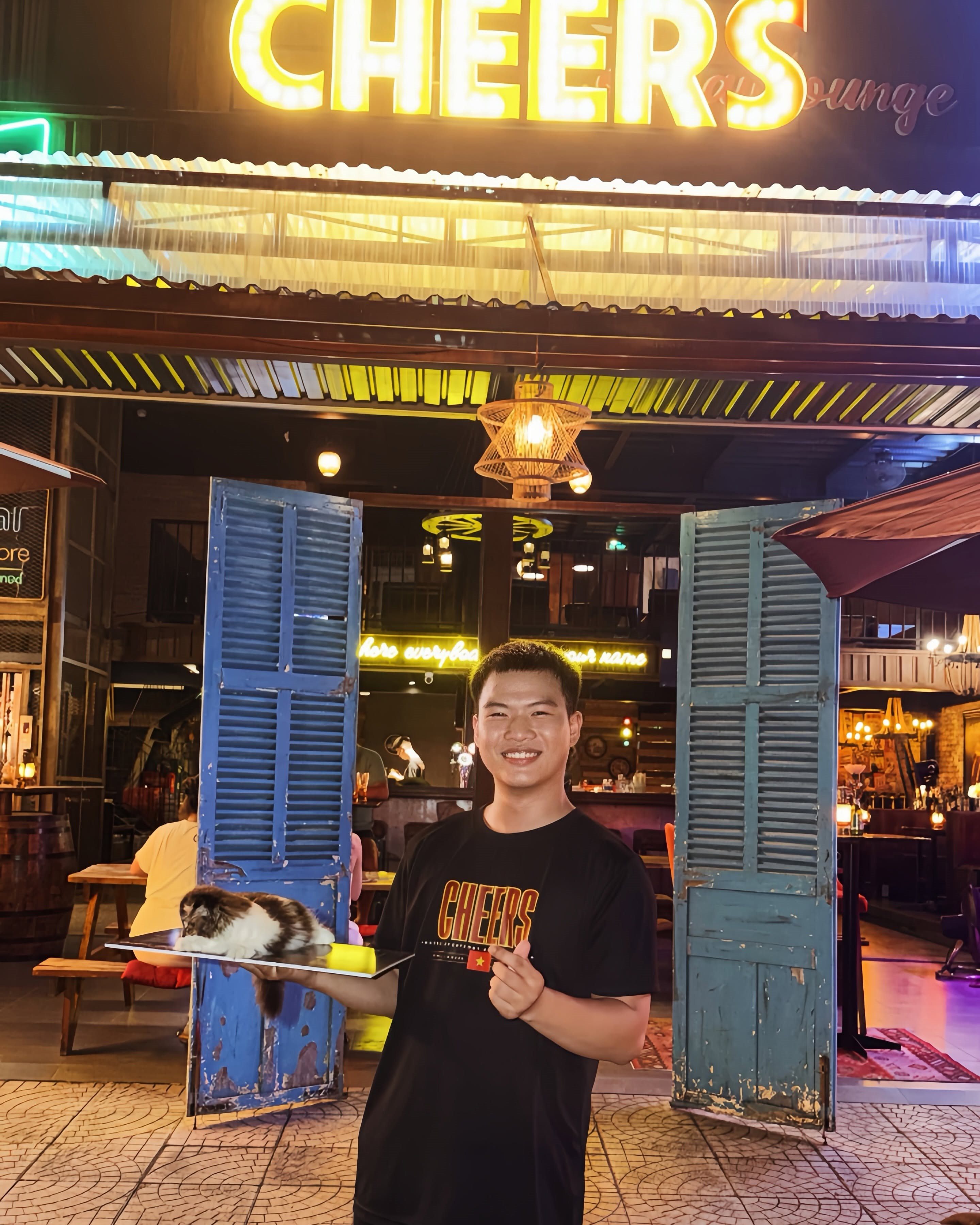 A smiling Cheers team member welcoming guests with the resident cat