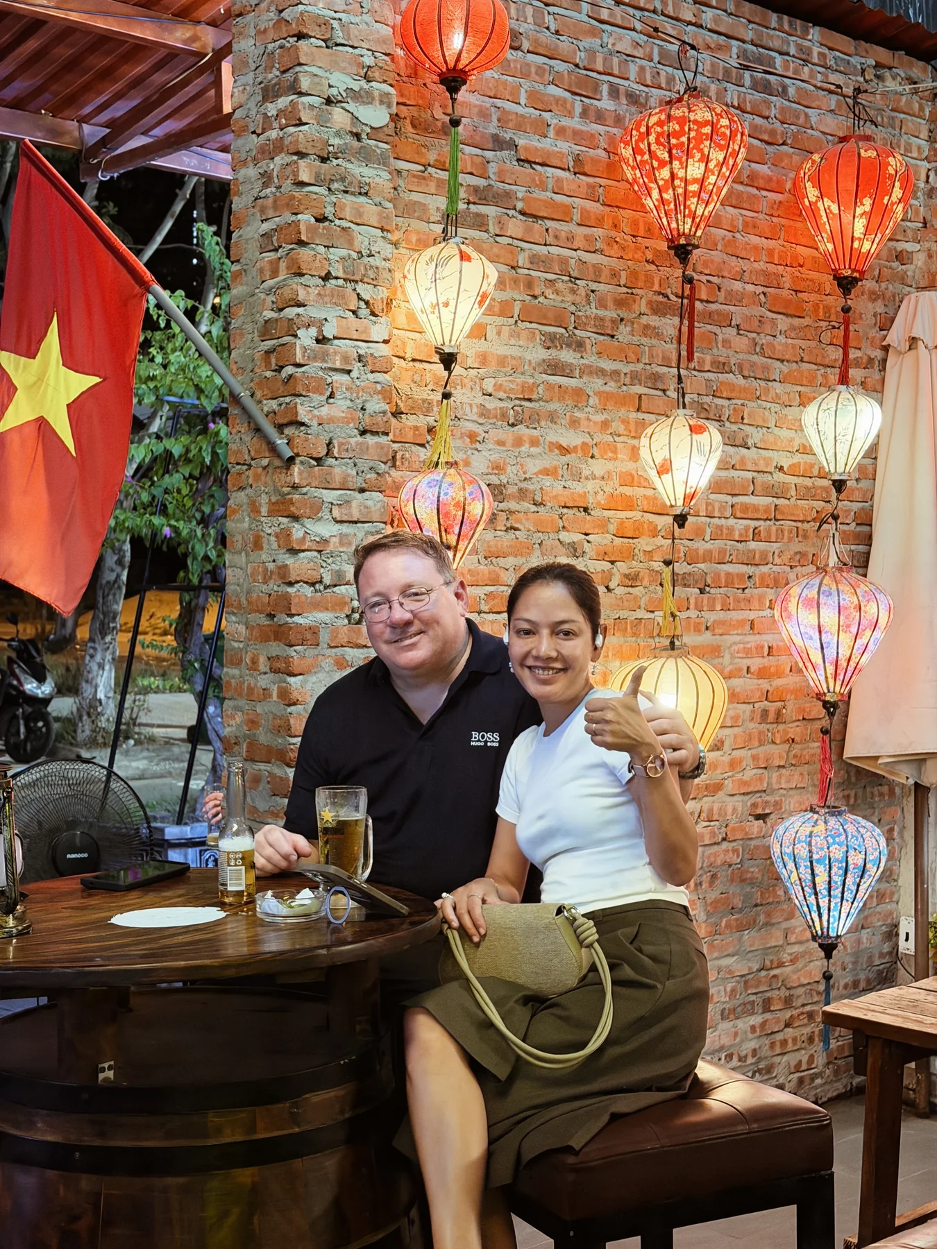 Two guests smiling together beside the brick wall at Cheers