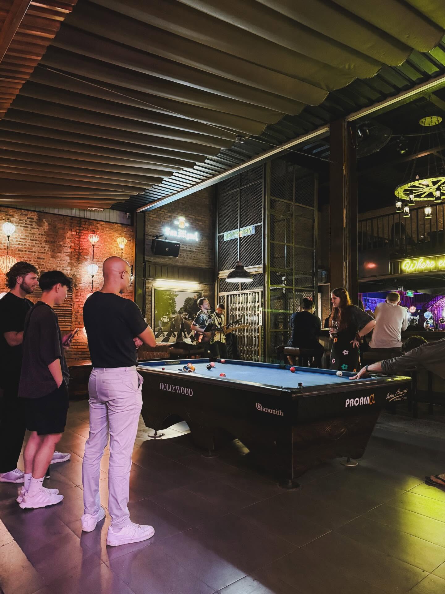 Guests playing pool while a musician performs at Cheers